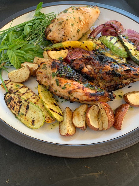 KATZ Honey Vinegar Marinated Grilled Chicken served on a white plate with grilled summer squash, red potatoes, and onions. Also on plate is a mix of fresh herbs including basil, parsley, and thyme.